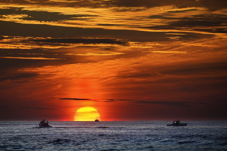 Soleil se couchant sur l'océan Atlantique avec des bateaux au premier plan.