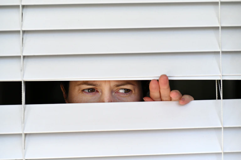 A person looking through gaps in venetian blinds