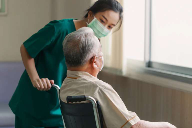 Aged care worker in a mask talks to an elderly patient in a wheelchair