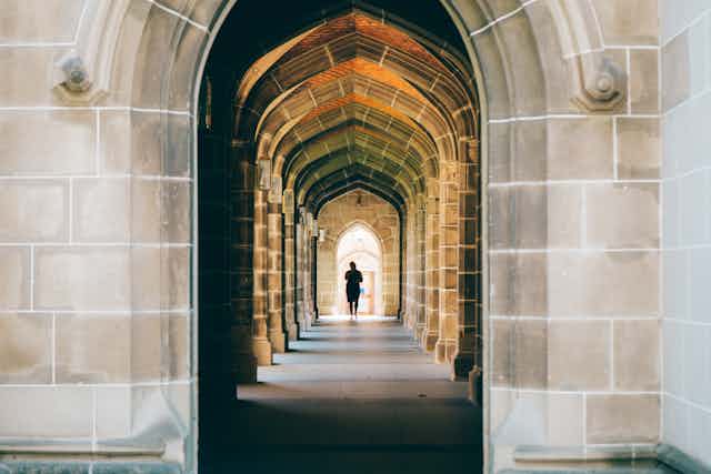 A student walks through a series of sandstone archways.