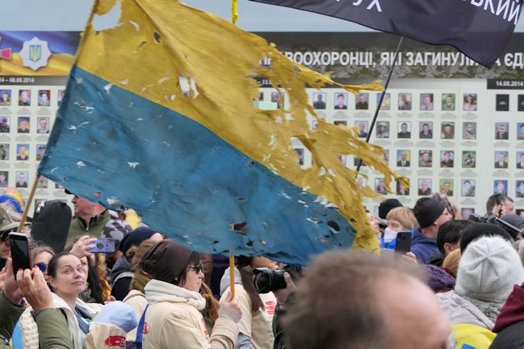 People stand in a square carrying a torn Ukrainian flag