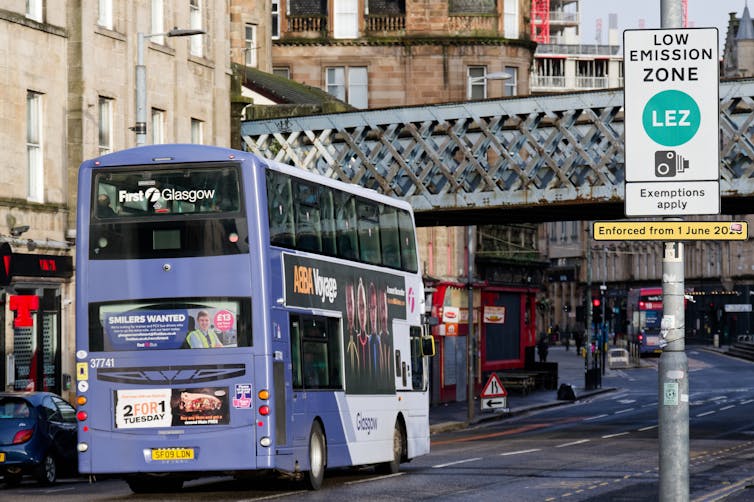 A purple bus passes under a railway bridge in Glasgow city centre.