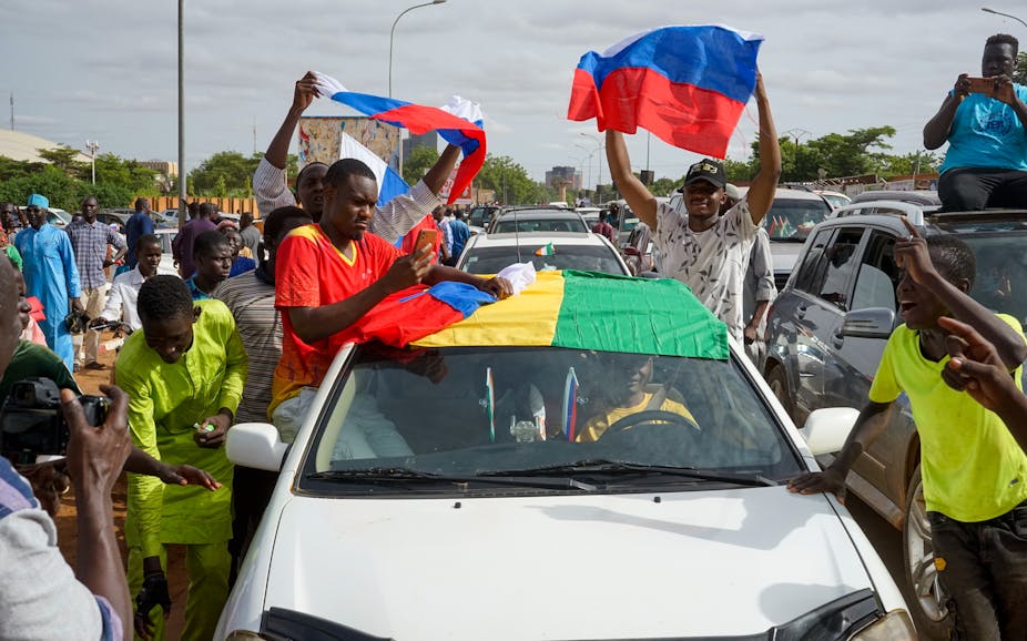 Nigeriens who support the coup sit on the windows of their car while waving Russian and Nigerien flags