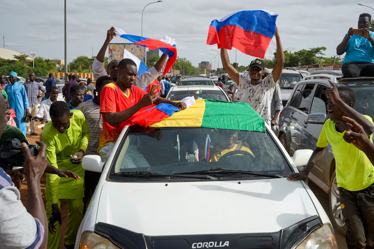 Nigeriens who support the coup sit on the windows of their car while waving Russian and Nigerien flags