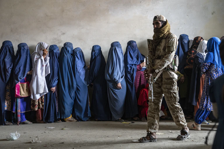 A heavily armed soldiers stands guard over a row of women in blue niqabs