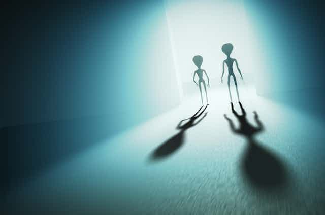 Shadows of two extraterrestrial beings are cut against the light