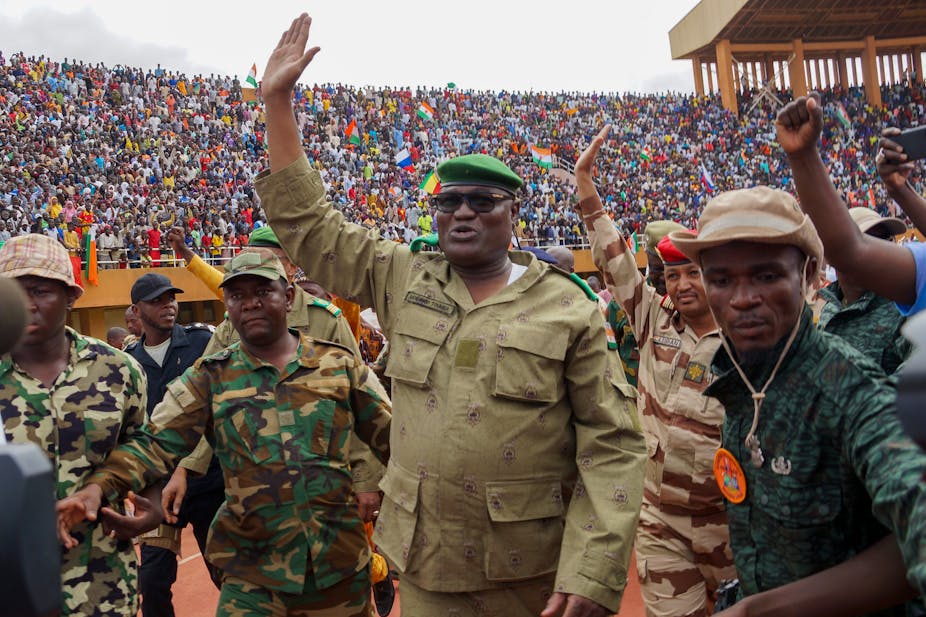 Men in military uniform wave at a large crowd in a stadium