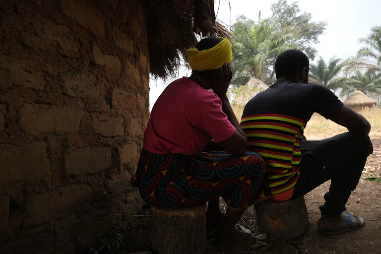 A man and woman seating on stumps by a hut