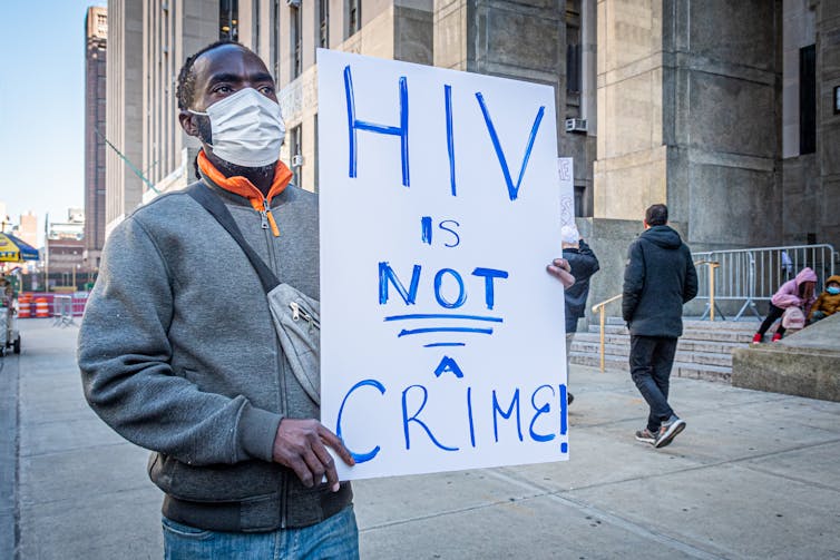A Black man is holding up a sign that says HIV is not a crime.