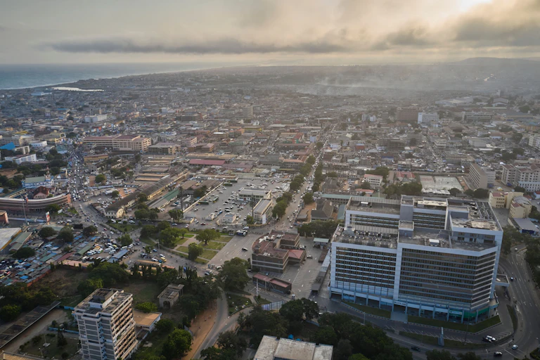 A high-up view of a city by a shoreline, with dusk rolling in.