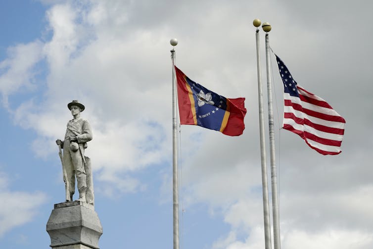 Two flags fly near a monument to a soldier.