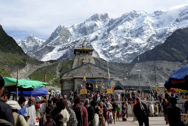 A long line of pilgrims outside a temple at the foot of snow-capped mountains.