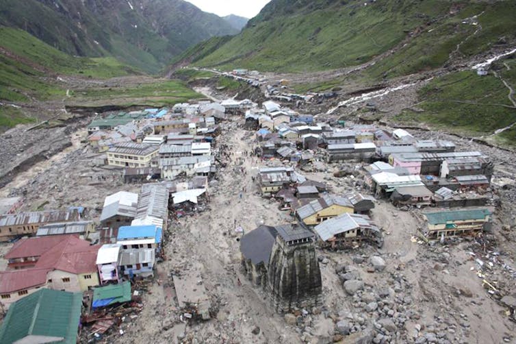 An aerial view showing buildings and erosion as a result of flooding in a town, located in a valley.