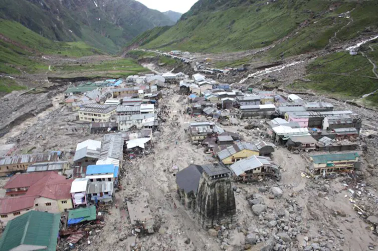 An aerial view showing buildings and erosion as a result of flooding in a town, located in a valley.
