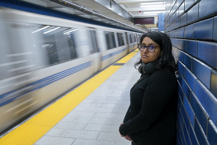 A woman stands on an otherwise empty subway station.