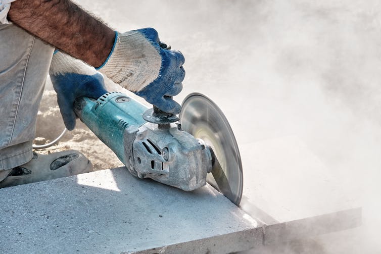 Hands of a pavement construction worker using an angle grinder for cutting the tiles.