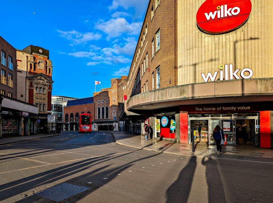 Bright blue sky behind a high street with a red bus, a few people and a branch of Wilko on the corner with two signs saying "Wilko" and "The home of family value".