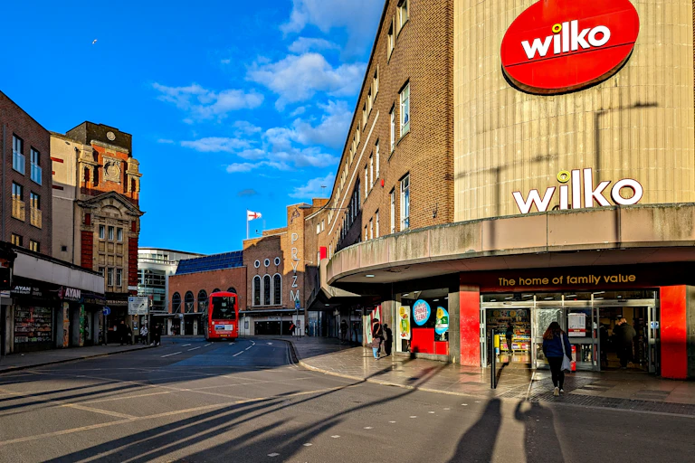 Bright blue sky behind a high street with a red bus, a few people and a branch of Wilko on the corner with two signs saying "Wilko" and "The home of family value".