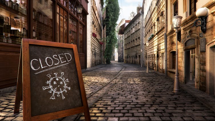 Quiet cobbled street with blackboard in the foreground that says 'Closed' with an image of a virus.