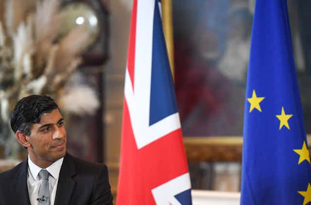 Rishi Sunak in front of a British flag and a European flag.