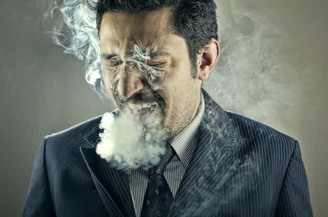 A man in a suit surrounded by smoke from cigarrettes.