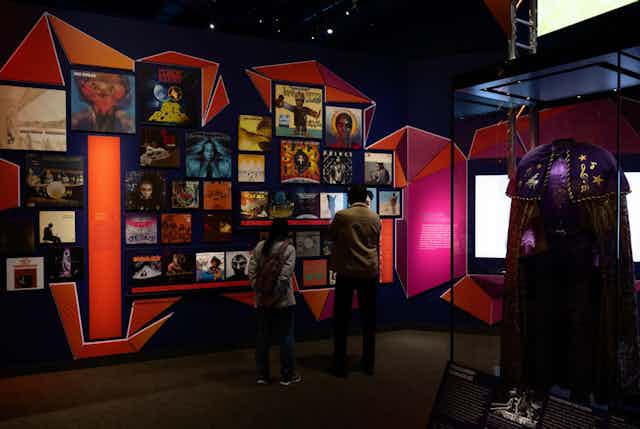 A dark room with a brightly-lit exhibit of images attached to pink and orange walls.