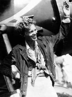 Black and white photo of woman smiling and waving in front of an airplane.