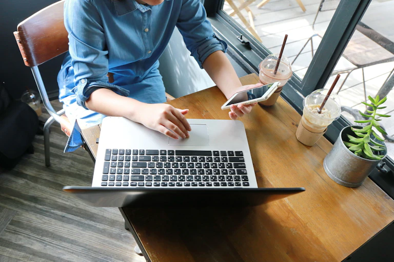 Woman holding smartphone, working on laptop, sitting at cafe table