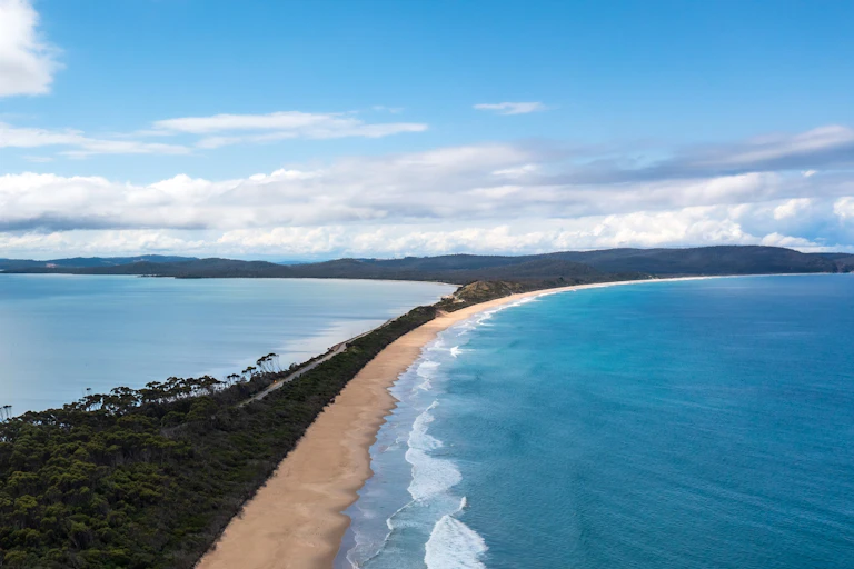 A photo showing a thin spit of land heading into the sea to distant hills.