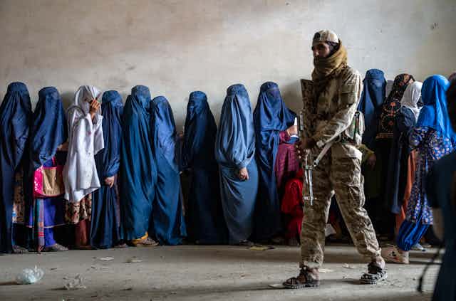 Un soldado fuertemente armado vigila una hilera de mujeres con niqabs azules