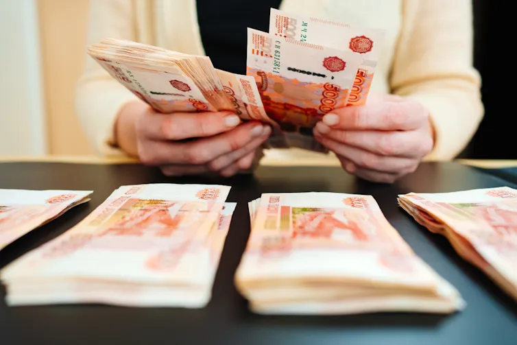 Hands counting Russian notes, piles of rouble-denominated notes on the table in foreground.