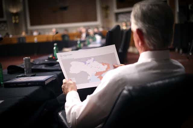 Un homme, assis, de dos, tenant dans ses mains une carte de l'Ukraine
