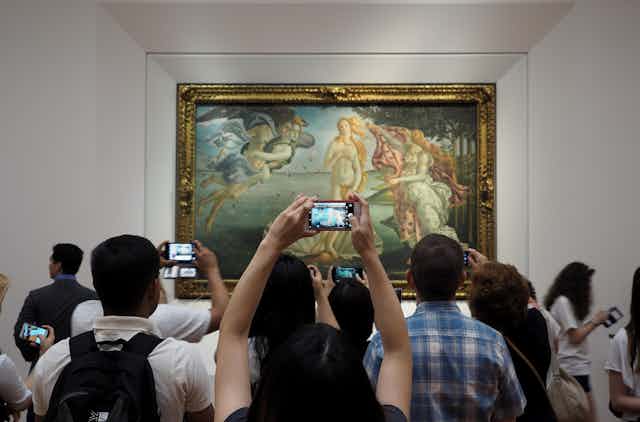 Turistas frente a un cuadro haciéndole fotos con el móvil.