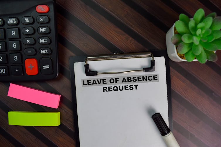 Overhead shot of desk with clipboard that says Leave of absence request, pen, calculator, post-its and potted plant.