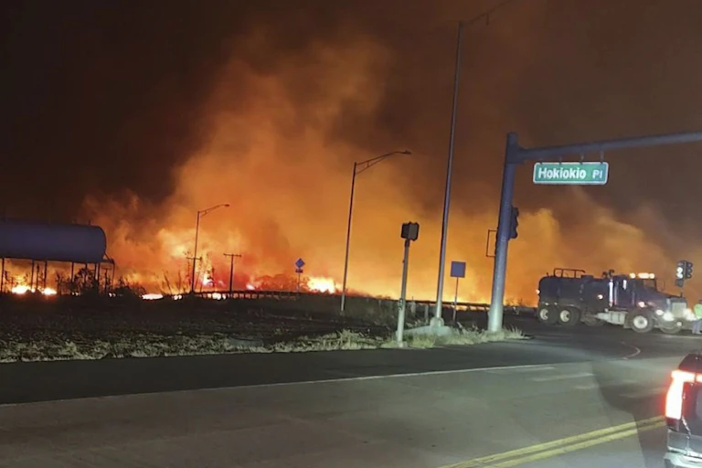 Flames line a road in the night as a water truck drives by.