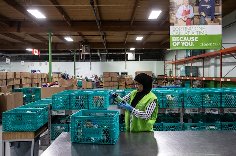 A woman in a hijab and green vest packs food into crates in a warehouse
