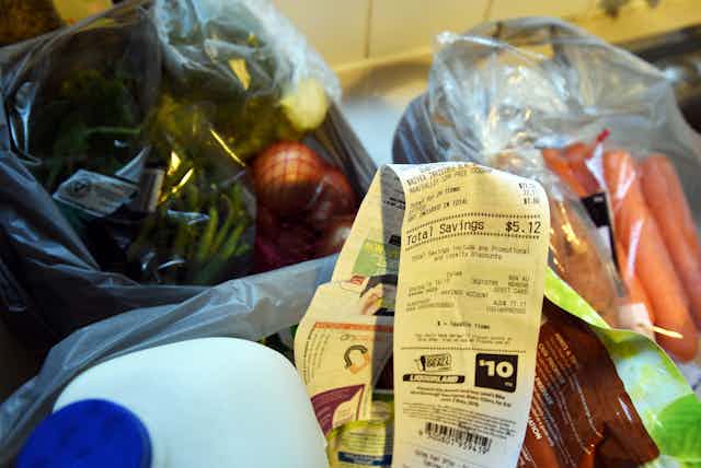 Groceries including milk, carrots and onions with a shopping receipt on a kitchen bench.
