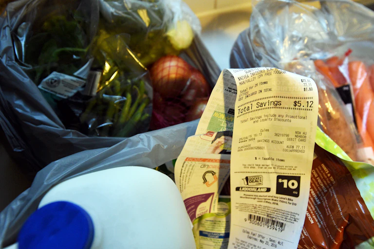 Groceries including milk, carrots and onions with a shopping receipt on a kitchen bench.