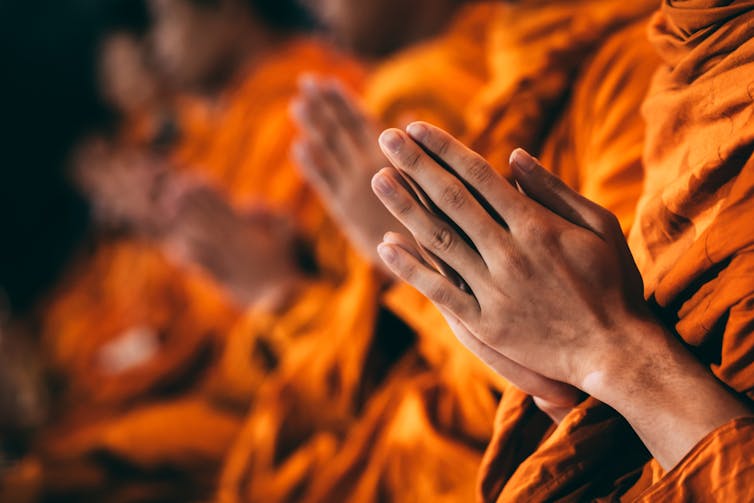 Monks wearing orange robes, palms together, chanting