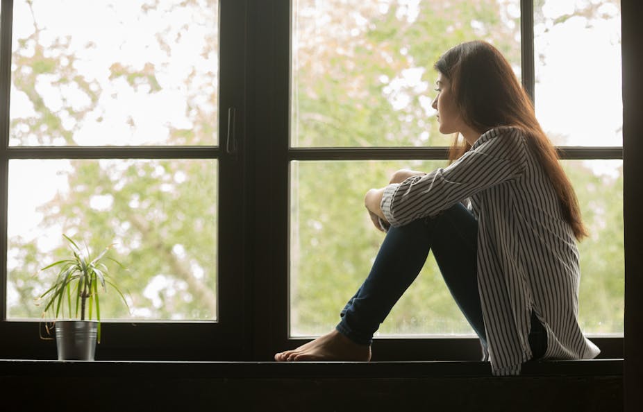 A woman sitting on a windowsill looking out of the window.
