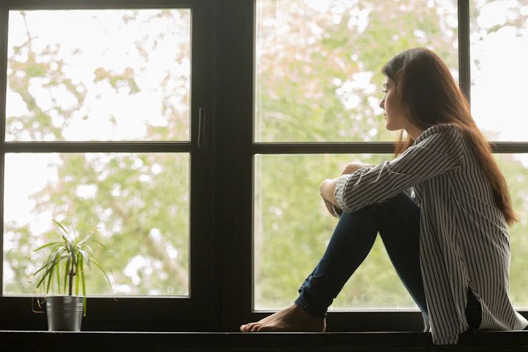 A woman sitting on a windowsill looking out of the window.