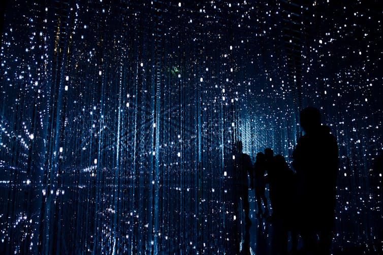 A constellation of lights in a dark room, with a group of people silhouetted against the light.