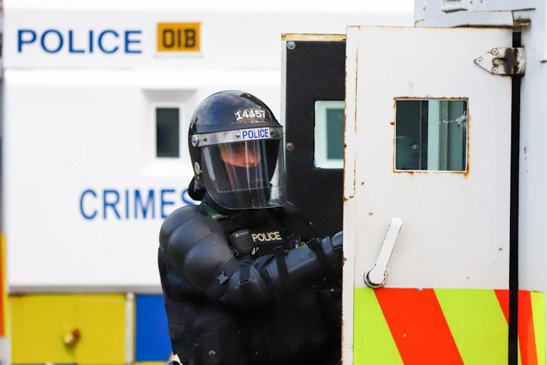 A PSNI officer in riot gear opening a van door.