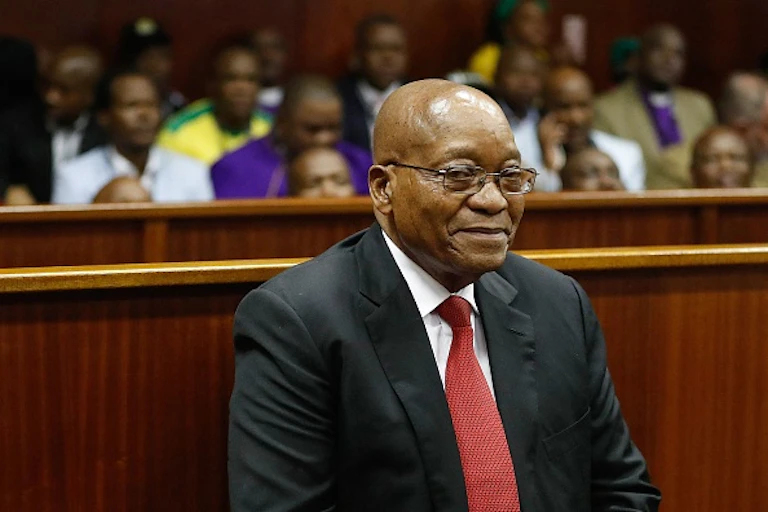 A man wearing a jacket, tie and specs smiles while sitting in the in court.