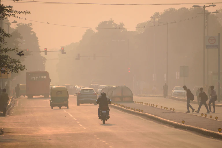 A polluted road with cars and a scooter driving down it.