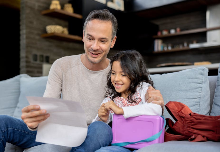 Father and young daughter sit on sofa looking at paper