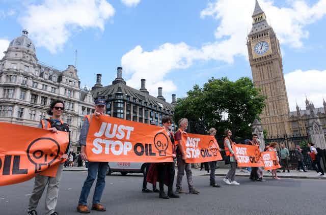A line of protestore holding Just Stop Oil banners, walking in front of the Houses of Parliament. 