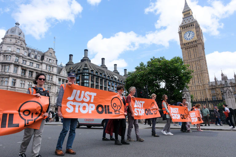 A line of protestore holding Just Stop Oil banners, walking in front of the Houses of Parliament.