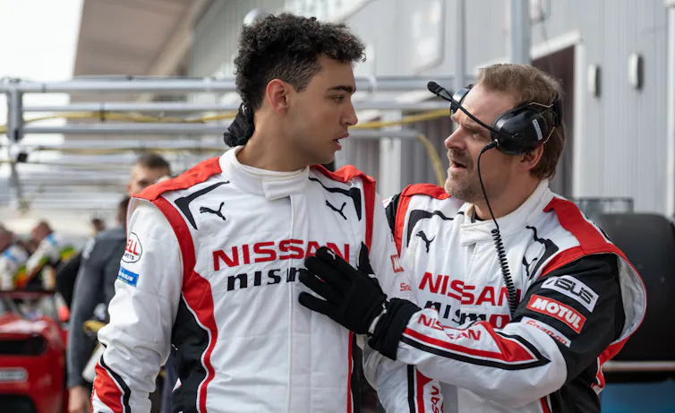 Archie Madekwe and David Harbour wearing white and red racing leathers.