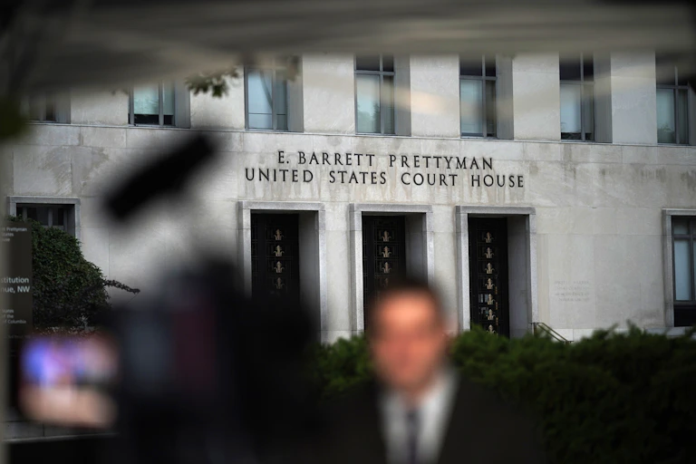 A fuzzy photo of a man in front of a big, gray building.